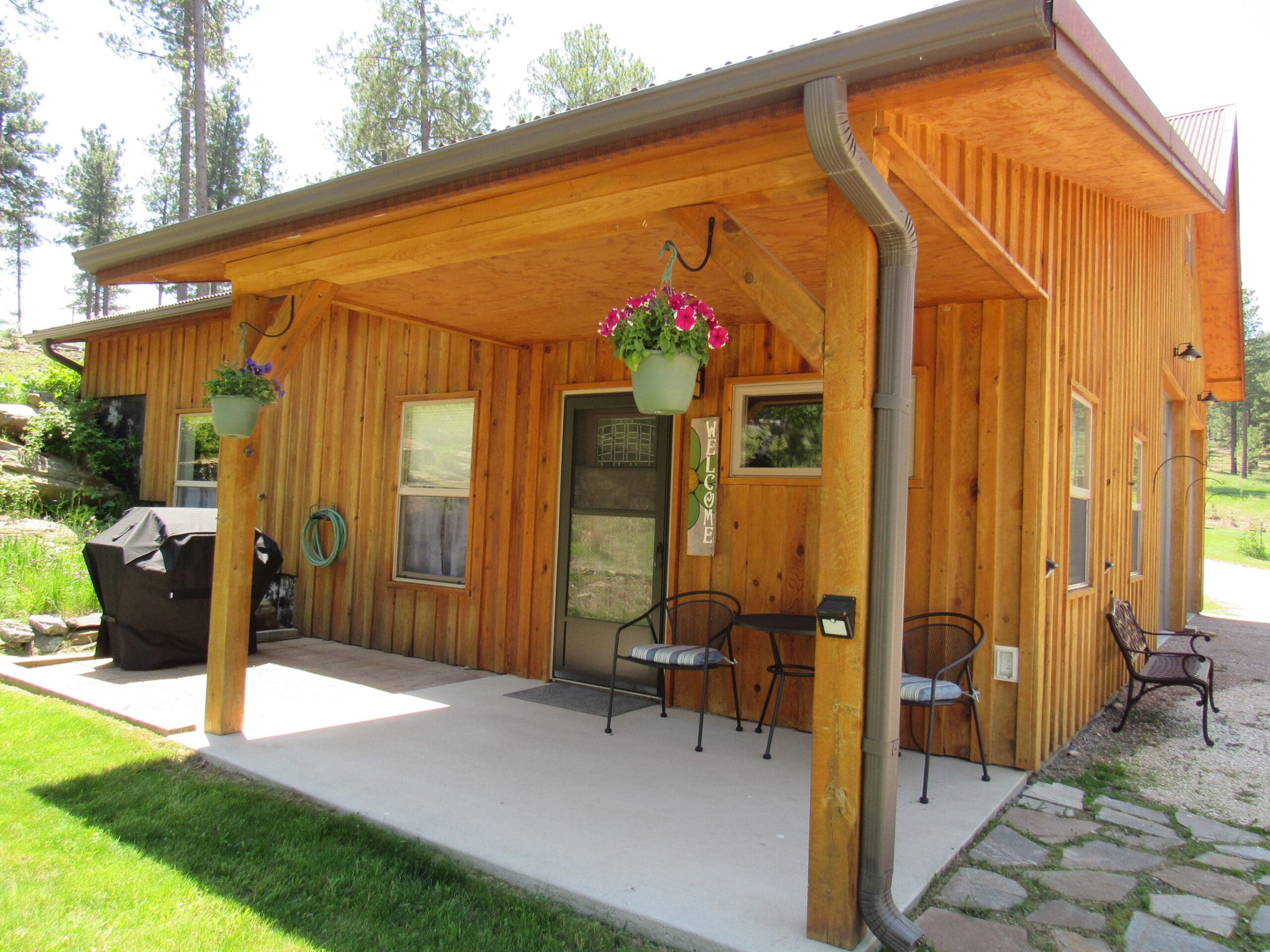 Front exterior of Aspen Acres Cabin in Rapid City, SD. The front gives off a rustic and homely feel with flower pots, a grill, a table and chairs outside.